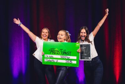 Tre glada studenter firar med diplom och prischeck på en scen