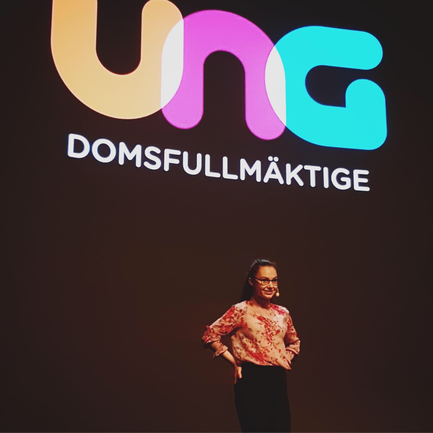 Elev föreläser på scen framför en stor skylt med texten 'UNG DOMSFULLMÄKTIGE'