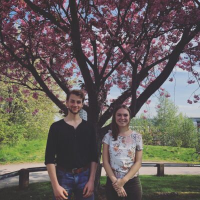 Två studenter står framför ett blommande körsbärsträd och ler