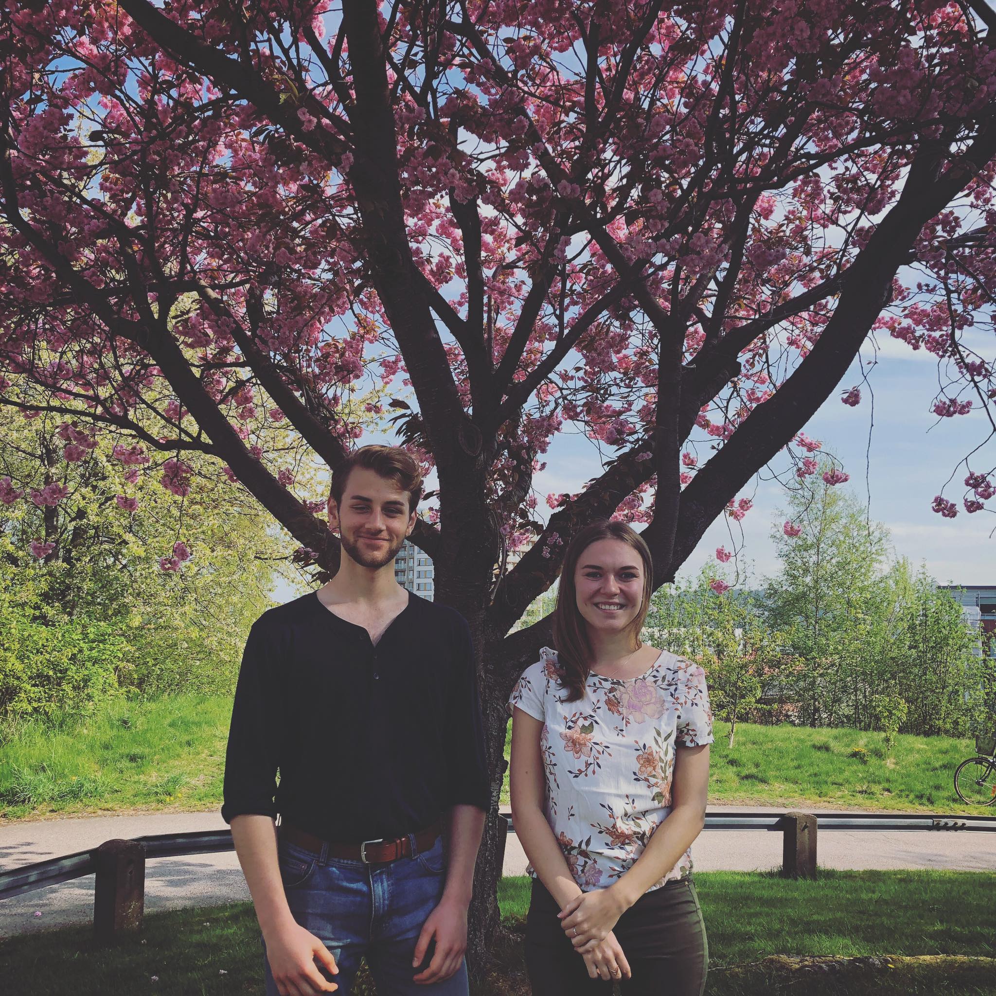 Två studenter står framför ett blommande körsbärsträd och ler