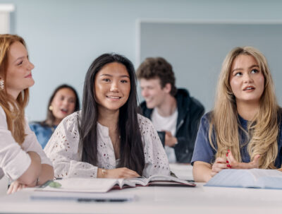 Elev sitter i klassrumet under en lektion och ler in i kameran.