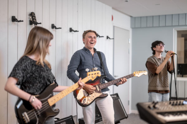 Glad kille står och spelar gitarr tillsammans med sina klasskompisar.